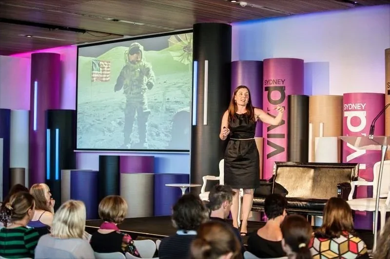 Michelle Williams presenting on stage at Vivid Ideas Sydney, gesturing toward a projection screen displaying a lunar mission image.